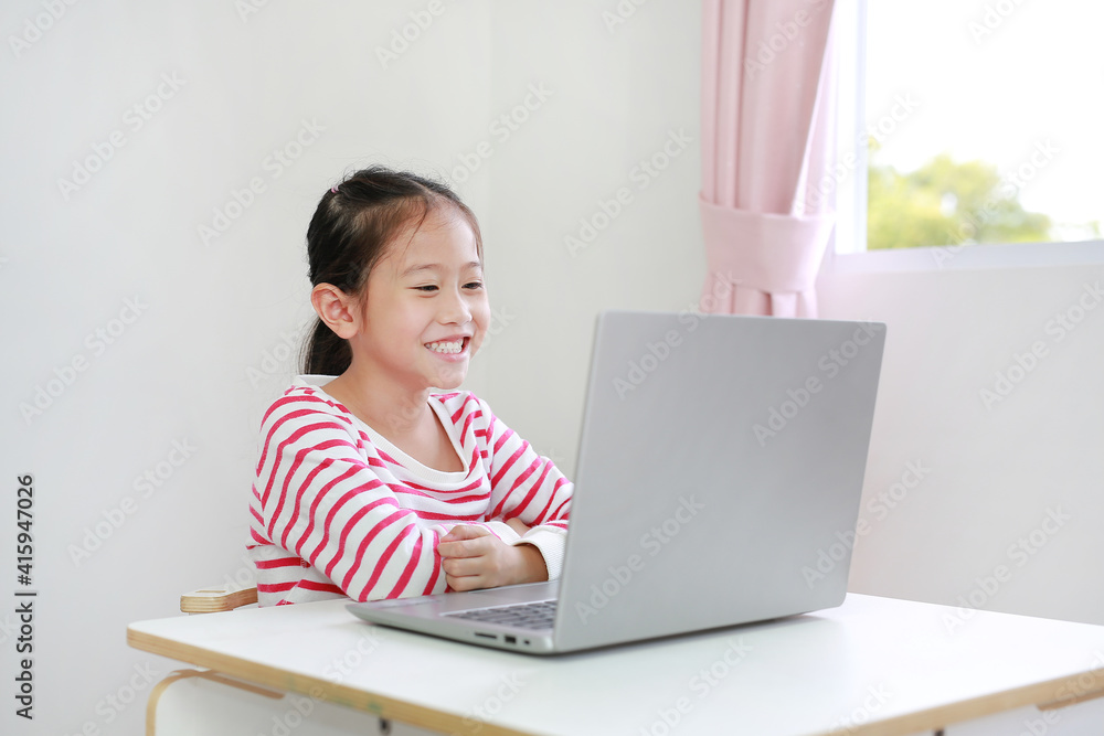Happy little Asian child girl sitting at desk and using laptop computer Happy little Asian child girl sitting at desk and using laptop computer