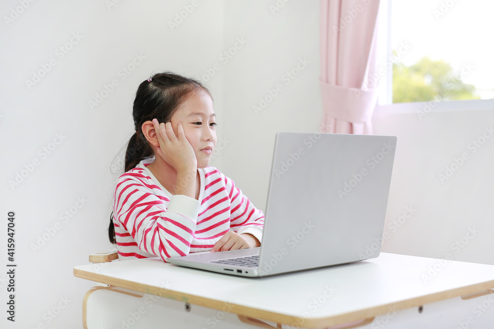 Happy little asian child girl sitting at desk and using laptop computer stay at home Happy little asian child girl sitting at desk and using laptop computer stay at home