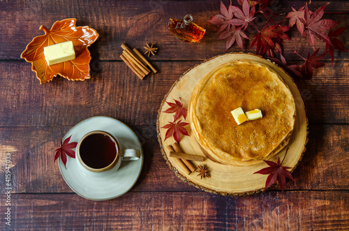 Thin Russian pancakes (crepes) with maple syrup and tea on a wooden table. Leaves, anise stars and cinnamon sticks are placed on the board as decoration. Autumn atmosphere.
