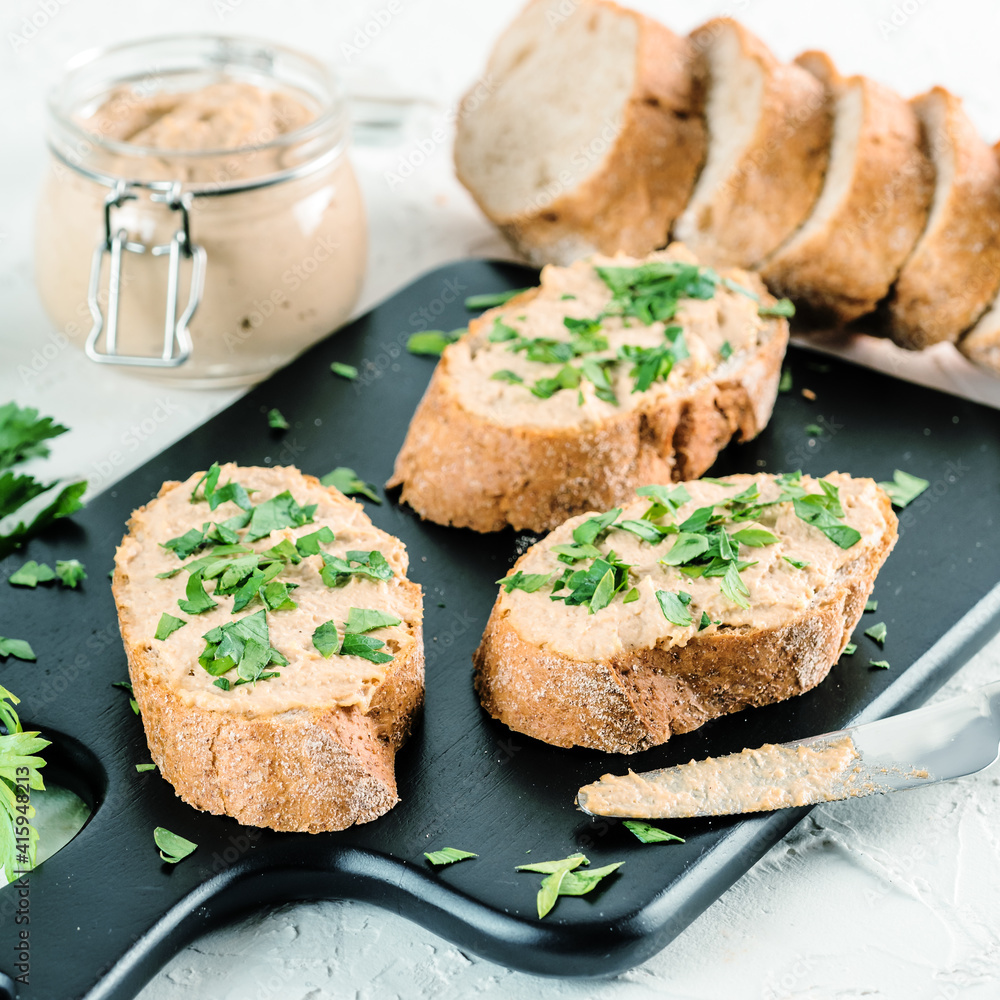 Close up view of slice bread with homemade turkey pate and fresh green parsley on black kutting board over white concrete background, Copy space. Close up view of slice bread with homemade turkey pate and fresh green parsley on black kutting board over white concrete background, Copy space.