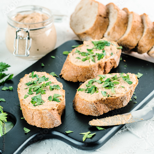 Close up view of slice bread with homemade turkey pate and fresh green parsley on black kutting board over white concrete background, Copy space.