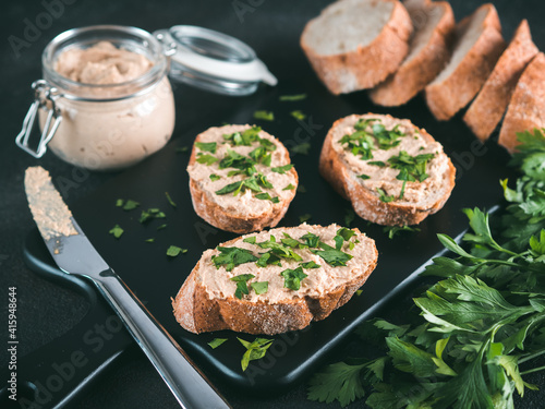 Close up view of slice bread with homemade turkey pate and fresh green parsley on black kutting board over black cement background, photo