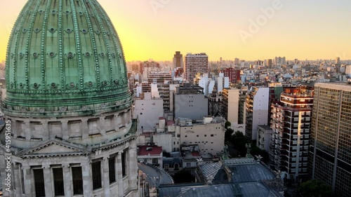 Aerial dolly in flying near green bronze dome of Argentine Congress building surrounded by Buenos Aires buildings at sunset photo