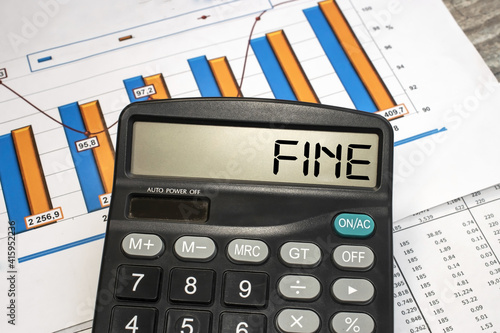 The word penalty is written on the monitor of a black calculator that lies against the background of business documents with a color chart. Business and financial concept