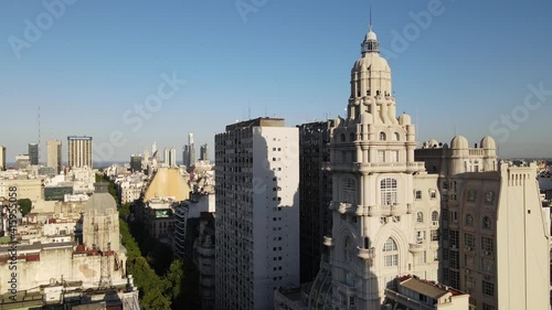 Aerial dolly out of Barolo Palace tower and tree-lined Avenida de Mayo surrounded by Buenos Aires buildings at sunset photo