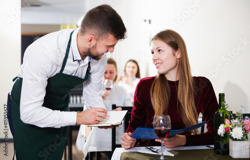 Welcoming waiter is taking order from cheerful woman in restaurante indoor.