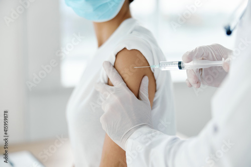 woman in medical mask doing coronavirus vaccine and doctor with syringe in hands