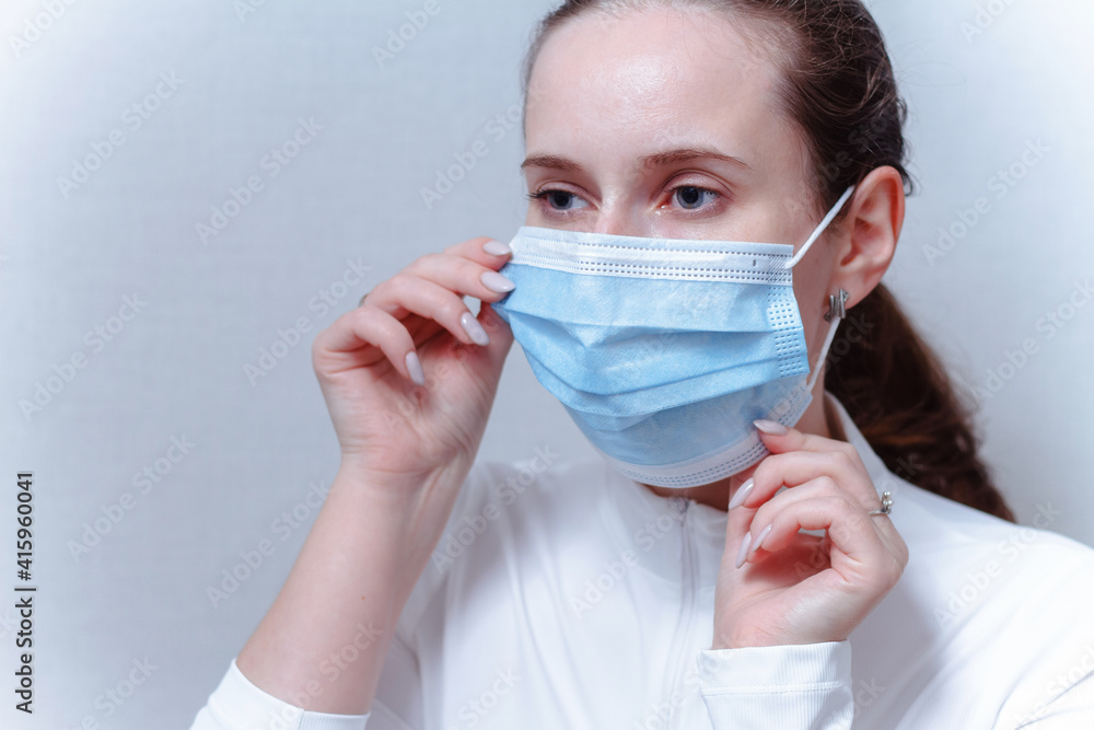 Young woman putting on face mask on a gray background.