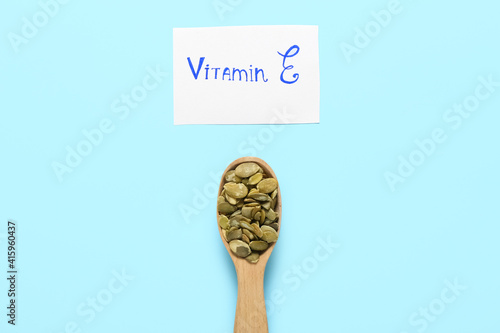 Text VITAMIN E and spoon with pumpkin seeds on color background photo