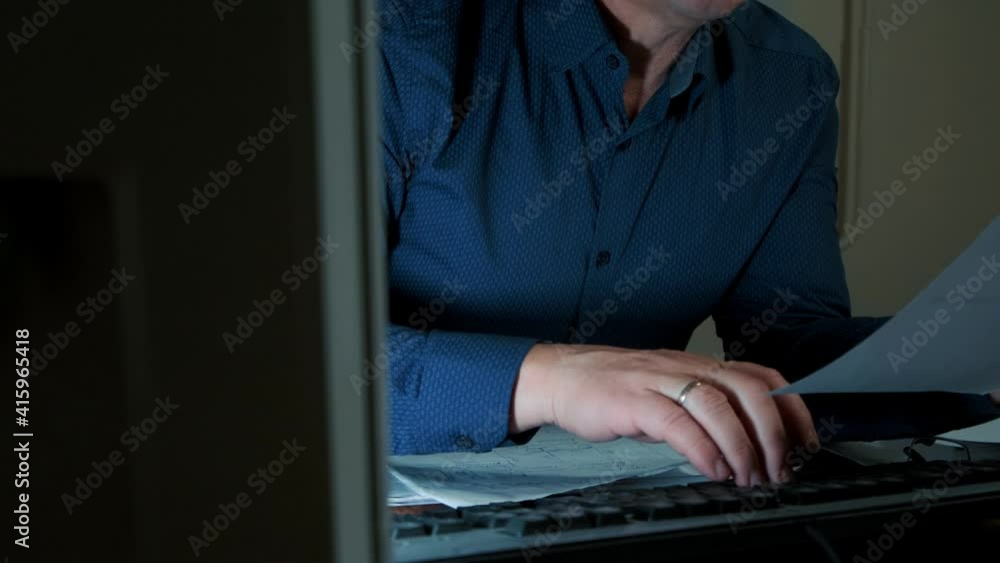 a man works at night in the office at the computer, typing on the keyboard a man works at night in the office at the computer, typing on the keyboard
