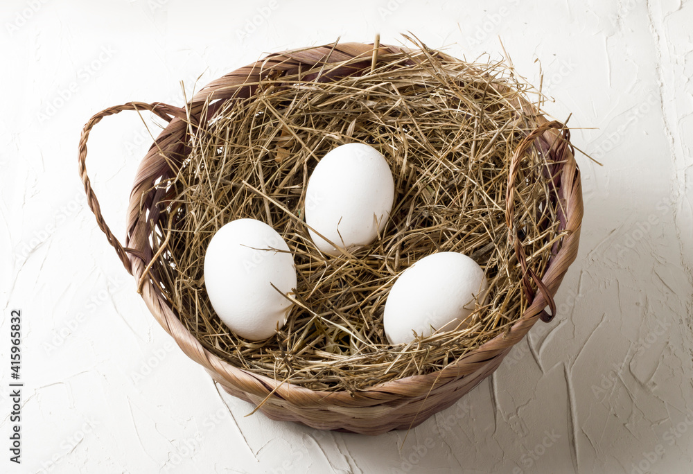three white chicken eggs in a hay nest on a white background