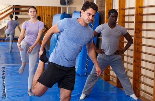 Woman and two men practicing stretch exercises in fitness center
