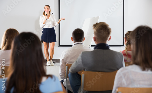 Friendly female teacher lecturing to attentive adult students at auditorium..
