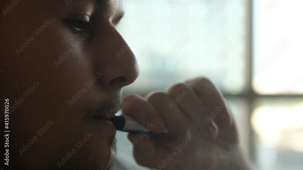 Close-up of man inhaling an e-cigarette vaping device. slow motion