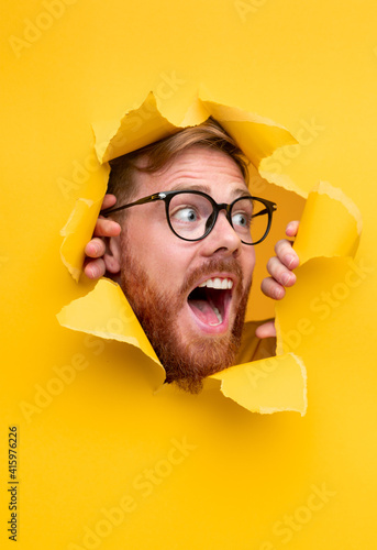 Excited man in glasses looking through torn paper hole