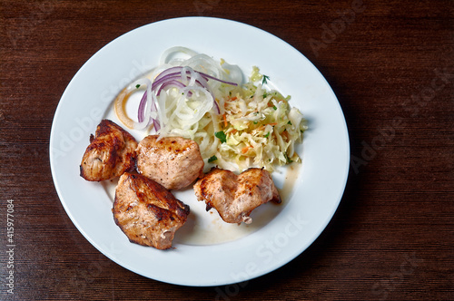 shish kebab with salad and onions on a white plate on a dark background