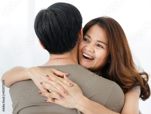 Horizontal back view portrait of senior Asian husband hugging his wife. A lovely couple standing closely and embracing each other with a warm hug. Concept of a romantic relationship in elderly