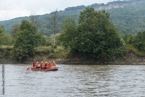People in life jackets are rafting down the river in a rubber boat