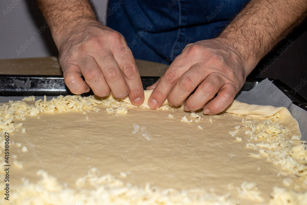 The hands of the cook who put grated cheese on the dough he rolls.