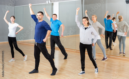 Adult females and males doing stretching workout before group dance training
