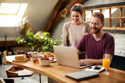 Happy couple using laptop after breakfast in dining room. © Drazen