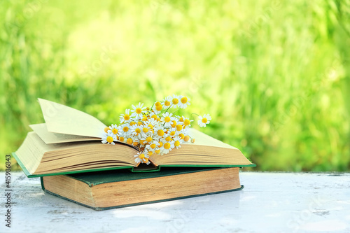 chamomile flowers bouqet and old books on table in garden. rustic summer nature background. concept of reading, relaxation, summer season