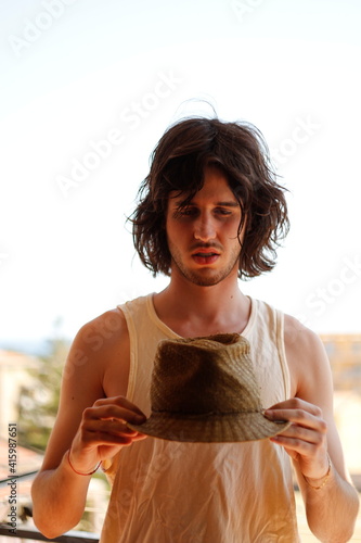 Ragazzo con capelli lunghi e cappello di paglia in mano photo