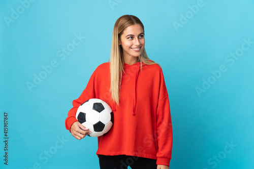Young football player woman isolated on blue background looking side