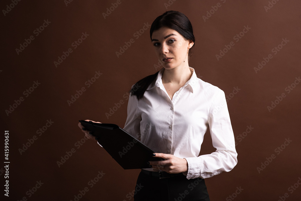 Serious brunette business woman with folder in hands on brown background in studio with copyspace Serious brunette business woman with folder in hands on brown background in studio with copyspace