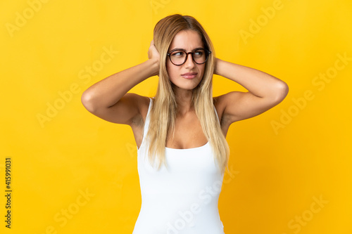 Young blonde woman isolated on yellow background frustrated and covering ears