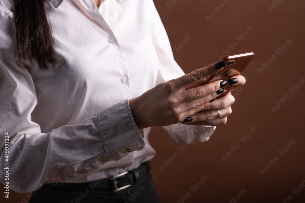 Closeup of a business woman's hands holding a smartphone in the studio on a brown background