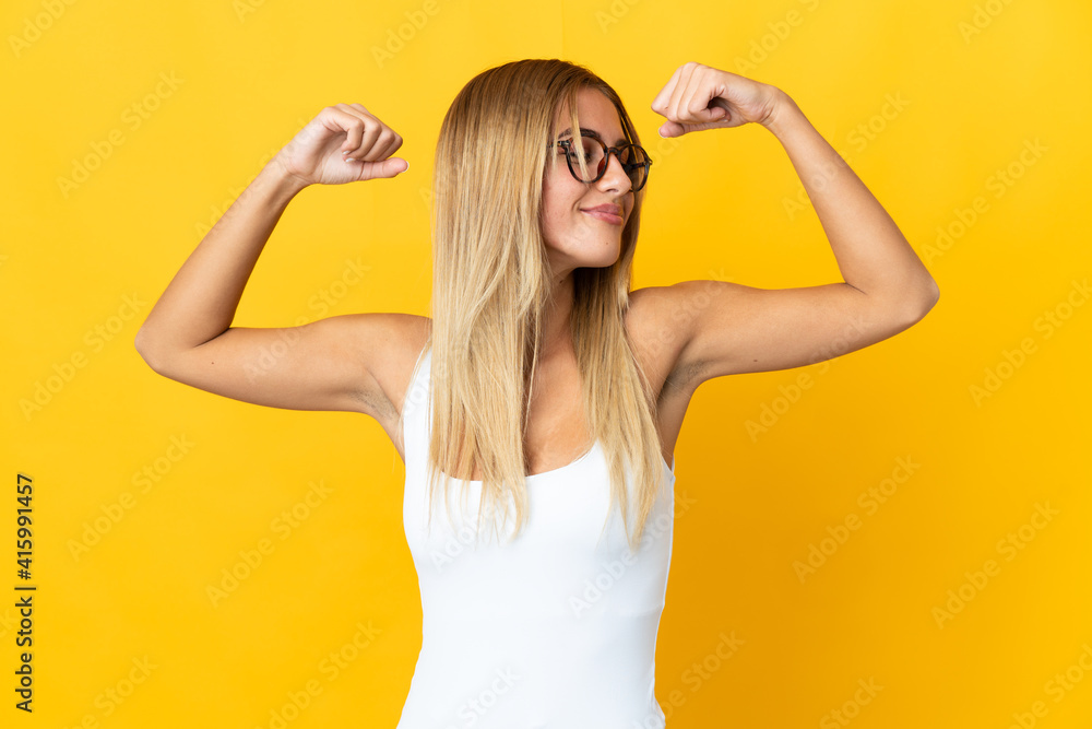 Young blonde woman isolated on yellow background doing strong gesture Young blonde woman isolated on yellow background doing strong gesture
