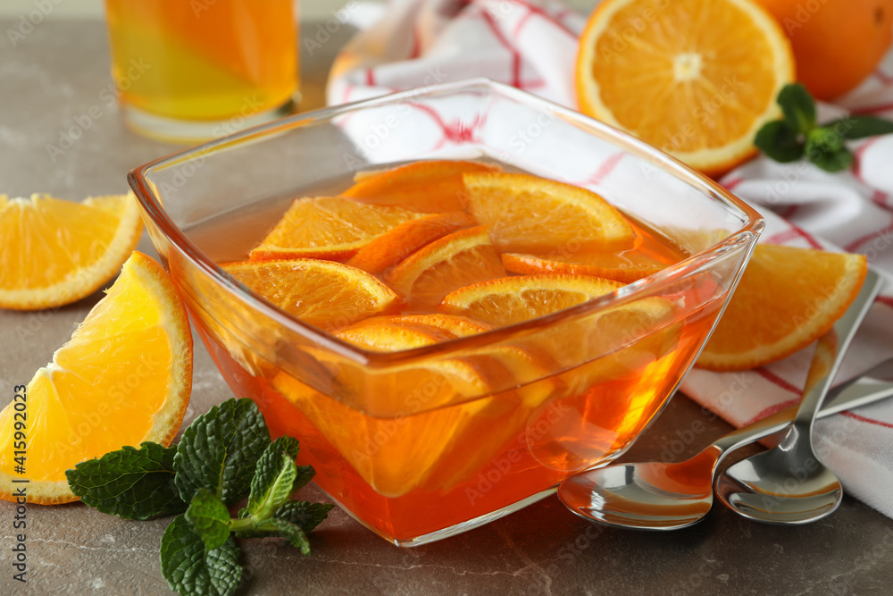 Concept of dessert with bowl of orange jelly with orange slices on gray table Concept of dessert with bowl of orange jelly with orange slices on gray table