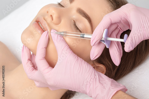 Cosmetologist does injections for lips augmentation and anti wrinkle in the nasolabial folds of a beautiful woman. Women's cosmetology in the beauty salon.