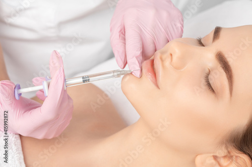 Cosmetologist does injections for lips augmentation and anti wrinkle in the nasolabial folds of a beautiful woman. Women's cosmetology in the beauty salon.