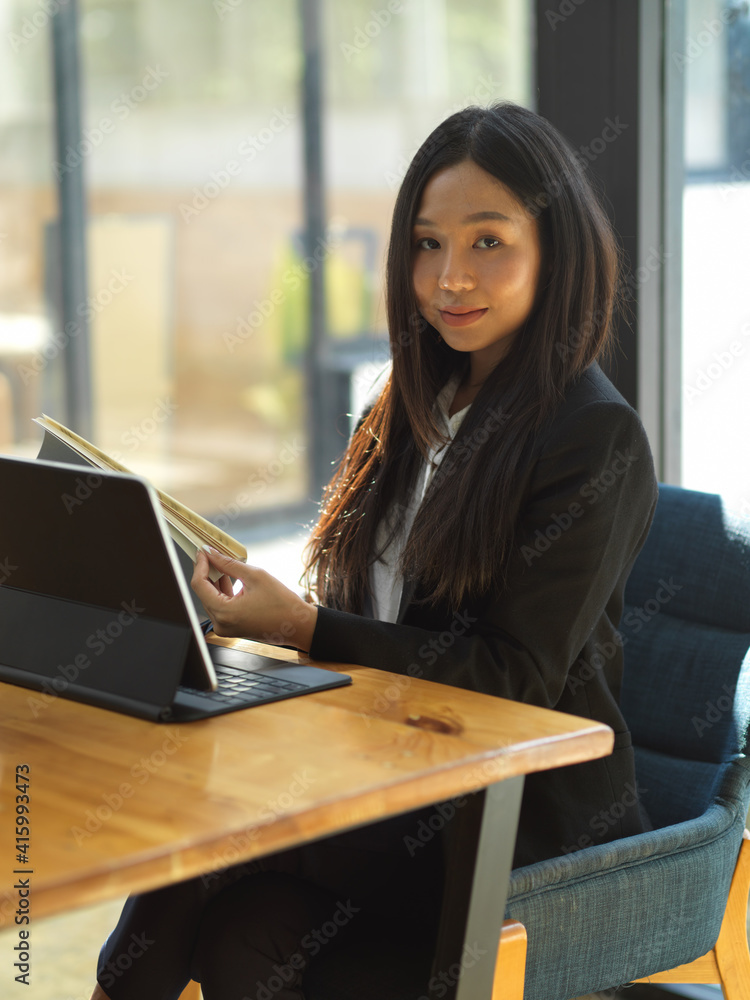 Businesswoman looking to camera while working with document file and digital tablet Businesswoman looking to camera while working with document file and digital tablet