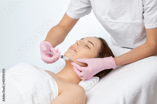 Cosmetologist makes lipolytic injections to burn fat on the chin  cheeks and neck of a woman against double chin. Female aesthetic cosmetology in a beauty salon.Cosmetology concept.