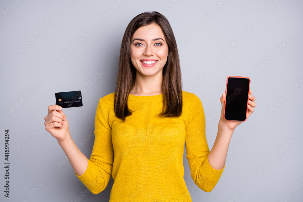 Portrait of pretty content cheerful girl holding in hands gadget bank card service isolated over grey color background Portrait of pretty content cheerful girl holding in hands gadget bank card service isolated over grey color background