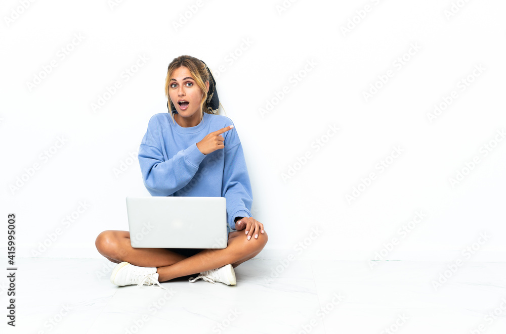 Young blonde Uruguayan girl with the laptop isolated on white background surprised and pointing side Young blonde Uruguayan girl with the laptop isolated on white background surprised and pointing side