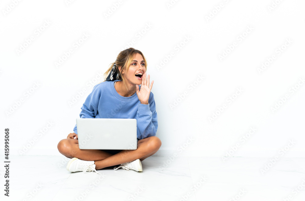 Young blonde Uruguayan girl with the laptop isolated on white background shouting with mouth wide open to the lateral Young blonde Uruguayan girl with the laptop isolated on white background shouting with mouth wide open to the lateral