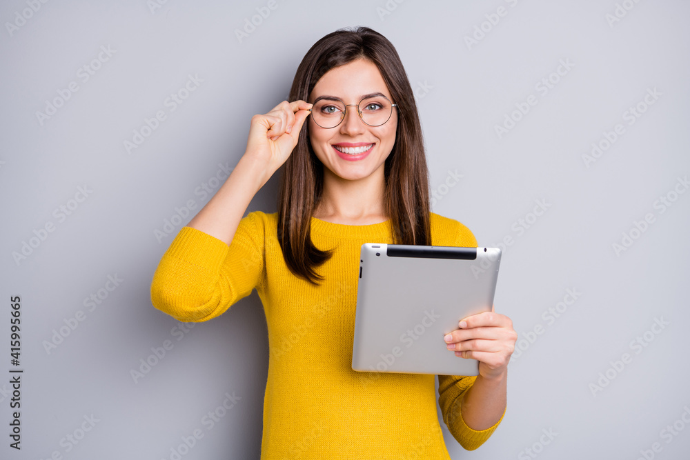 Portrait of charming content cheerful girl holding in hands using tablet touching specs isolated over grey color background Portrait of charming content cheerful girl holding in hands using tablet touching specs isolated over grey color background