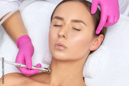 The cosmetologist makes the procedure Microdermabrasion of the face skin and neck of a beautiful girl in a beauty salon.Cosmetology and professional skin care.