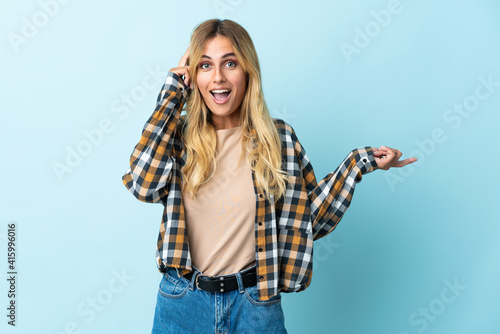 Young blonde Uruguayan isolated on blue background surprised and pointing finger to the side