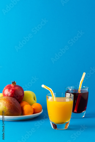 Delicious sweet citrus, mango and pomegranate juices in glasses and ripe fruits on a blue background