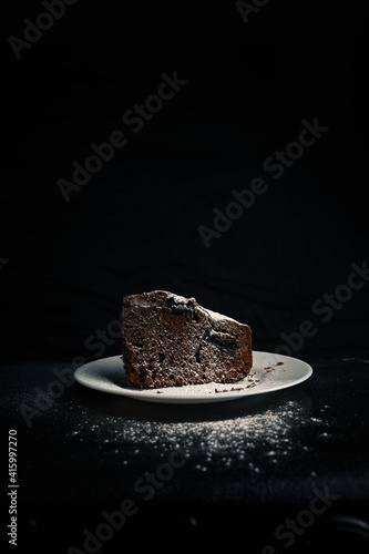 Chocolate pie on a white plate with a sugar powder on top on the black background.