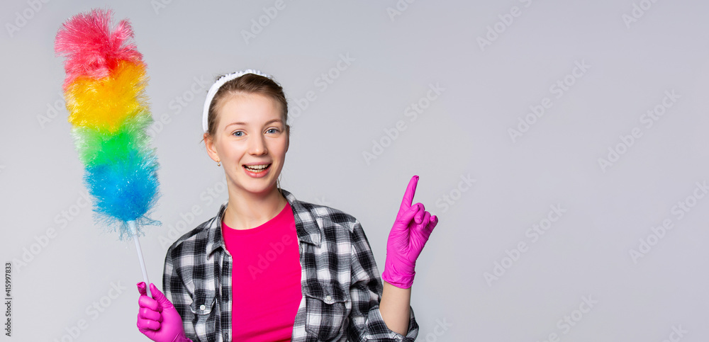 Portrait of housewife who is ready for housework with raised forefinger to empty space. Banner- long format, gray background
