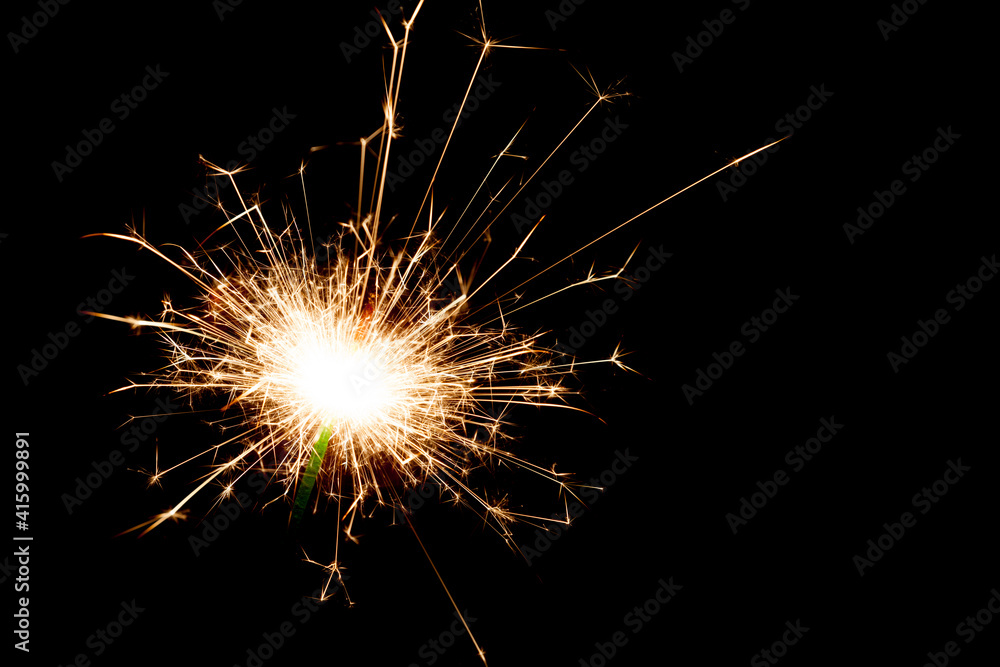 Close-up on a sparkler lit in the dark with copy space on the right.