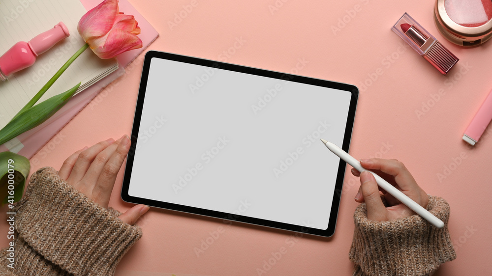 Female hands working with digital tablet on feminine workspace with cosmetics and flowers Female hands working with digital tablet on feminine workspace with cosmetics and flowers