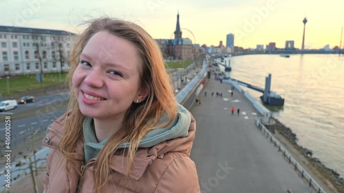 [4k] slow motion portrait of young woman smiling playing in her blonde hair with cityscape of Düsseldorf in Background in sunset