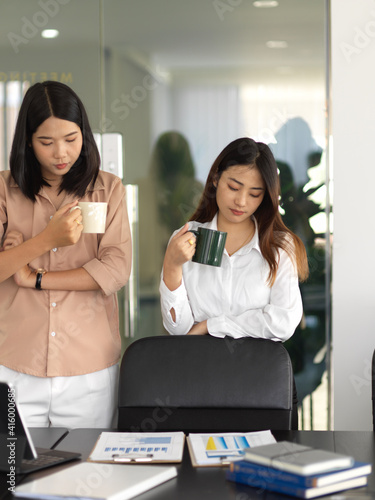 Two businesswomen taking a coffee break and reading business document in meeting room